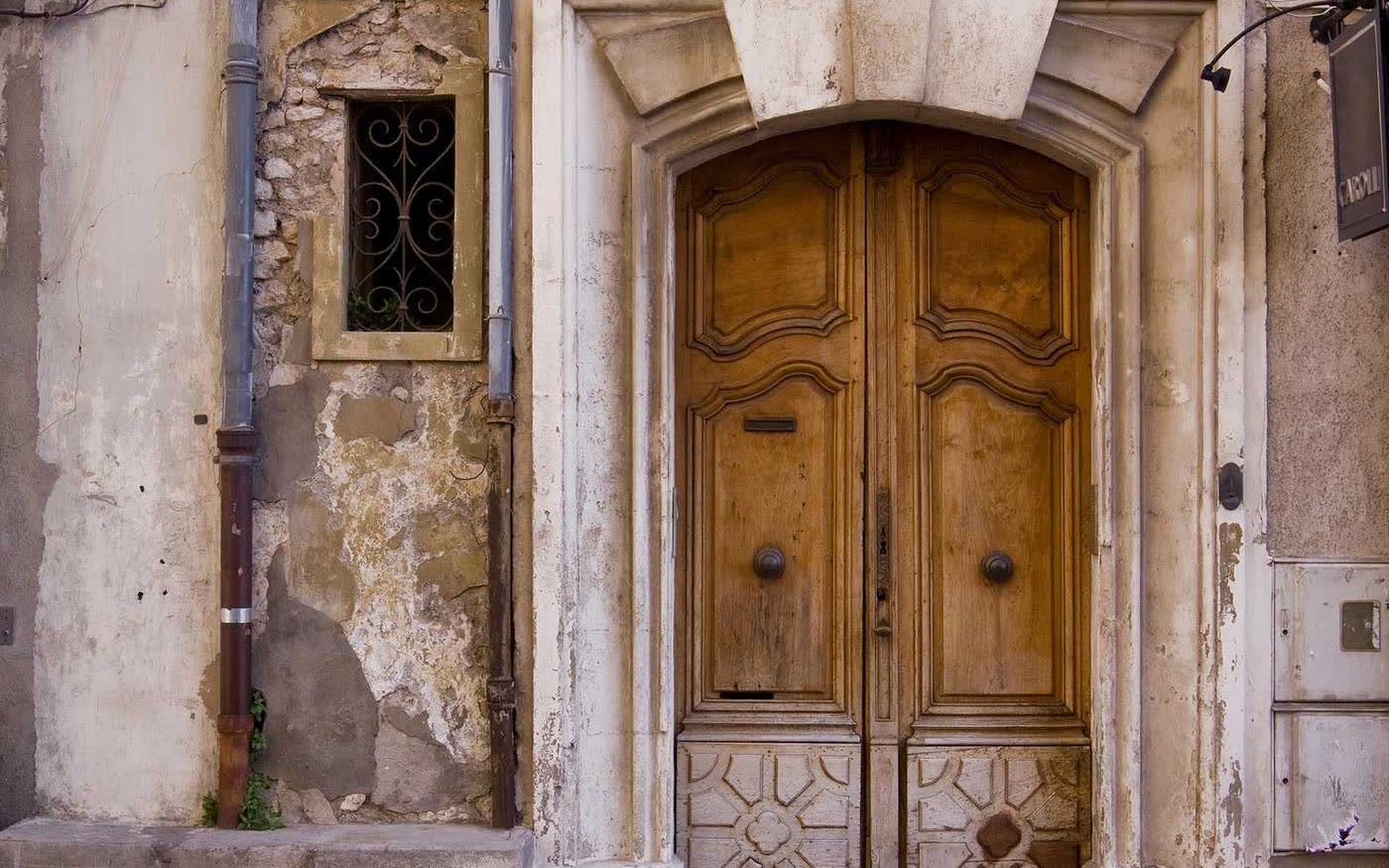 A tall carved wooden door, ochre and weathered, set in crumbling pale stone