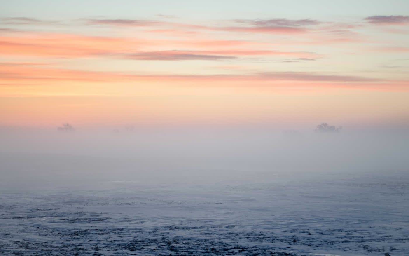 A pale pink and blue dawn over a flat, silent sea