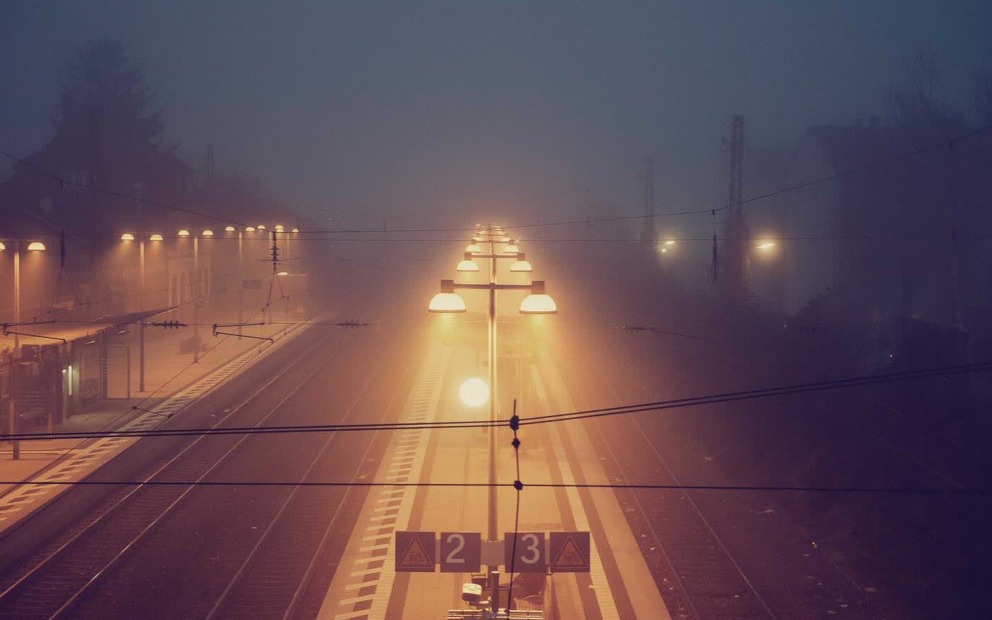 Station lamps burning through heavy amber fog, rails running away into the dark