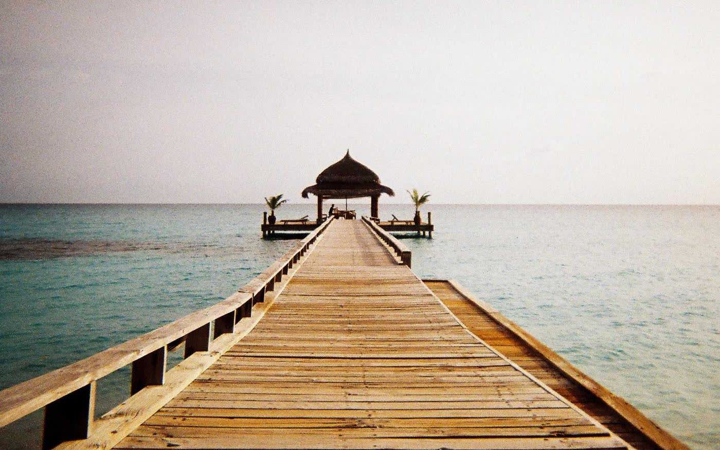 A wooden jetty running out over pale turquoise water to a small pavilion