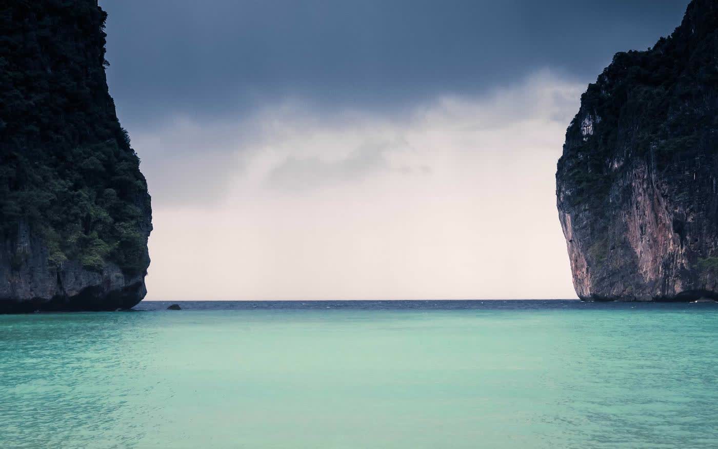 A turquoise lagoon between two dark limestone cliffs under a heavy sky